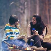 Two women talking and sitting on the ground by a fire