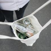 Person carrying empty glass bottles in a reusable bag