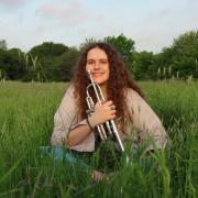 Anna Kallinikos, sitting in a field with her trumpet