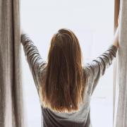 Person opening up curtains to let light into room