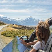 Person pulled over on side of a mountain road with a paper map in hand