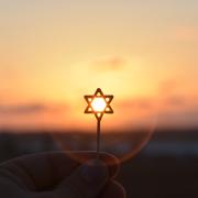 Person holds a small Jewish star in front of a setting sun