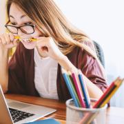 stressed out student bites pencil while looking at laptop computer