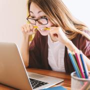 Awoman sitting at a computer biting a pencil in stress