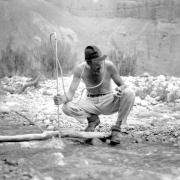 Man holding pole crouches in stream