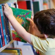 Child pulls a book from the shelf at the library