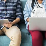 Man on tablet, woman on laptop sit next to each other