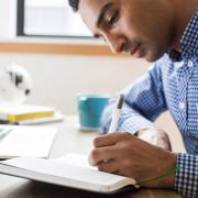 person writing in notebook and working on computer