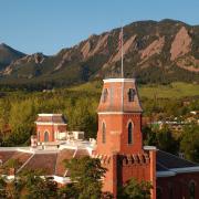 A bright sun reflects on the roof of Old Main and its surroundings, including the Flatirons in the background.