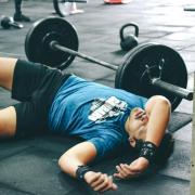 Person lies on gym floor, exhausted after lifting weights