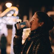 Woman sipping hot drink, looking at holiday lights