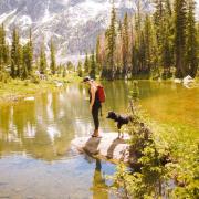 person and dog by a river with mountains in the background