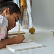 Photo of girl writing in notebook with tablet computer in the background