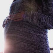 Pregnant woman in sweater rests hands on stomach