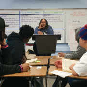 A teacher at a lectern speaks to students sitting at desks