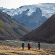 People walking toward a snow-covered mountain through a dry river bed of rocks.