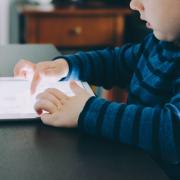 Child plays on tablet while sitting at table