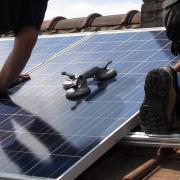 Workers install solar panels on a roof. 