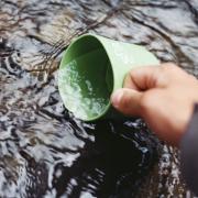 Woman dips drinking cup into fresh water source