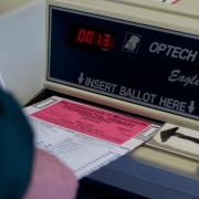 A person slides a ballot into an electronic voting machine.