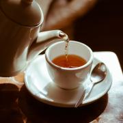 Tea is poured from a white kettle into a white cup. 