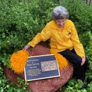 Peggy Coppom sits next to a plaque honoring her and her late twin sister, Betty Hoover. (Photo by Sarah Adderholt/University of Colorado)