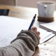 Person writing on paper with coffee mug in the background