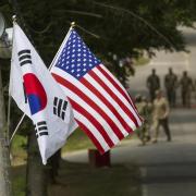 Republic of Korea and U.S. flags fly side by side, soldiers in background