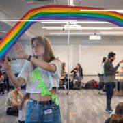 Student helps set up a workshop with rainbow painted on a window