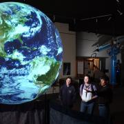 Community members look at huge, glowing model of Earth