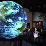 People look at an image of Earth projected on a sphere.