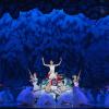 Ballerinas make a tiered circle formation on a stage lit in blue hues. 