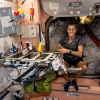 Woman wearing a t-shirt and shorts seated in a cluttered cabin aboard a space station
