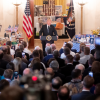 Donald Trump standing at a podium in front of a crowd of people in a hallway