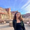 Jane Foreman stands outside with campus buildings and a bright blue sky above her.