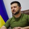 Ukrainian President Volodymyr Zelenskyy makes a speech in a green shirt, with the yellow and blue Ukrainian flag behind him. 
