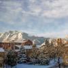 Campus buildings and the Flatirons in the background are frosted with snow, under a partly sunny sky—colors of blue brown and white.