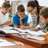 Teacher writes in a booklet in a classroom while four students look on