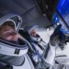 Two astronauts wearing open helmets sit inside a cockpit