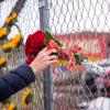 Person rests a bouquet of roses in a chainlink fence