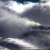 Snow flying off of a mountain top in the wind