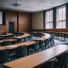 An empty lecture hall appears with rows of long, curved desks and black chairs.