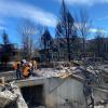 Three people in neon vests kneeling amid rubble from the Marshall Fire