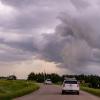 Two white SUVs drive down a single-lane highway in the country as gray storm clouds form overhead