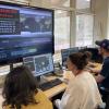 Three people seen from behind look at a large computer monitor
