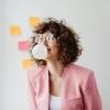 Woman blowing a bubble with gum near a board with sticky notes.