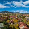 An aerial view shows a small Kittredge Pond on the CU Boulder campus, surrounded by terra cotta tiled roofs and colorful fall foliage from trees, with a bright blue sky and light clouds overhead.
