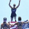 Melissa Stockwell, in stars-and-stripes track wear, with arms extended above her head, faces two people holding an American flag. (Wikimedia Commons/Tânia Rêgo/Agência Brasil)