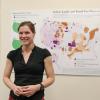 Grad student poses for photo in front of her research visualization board