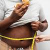 Person eats a burger while someone measures their abdomen